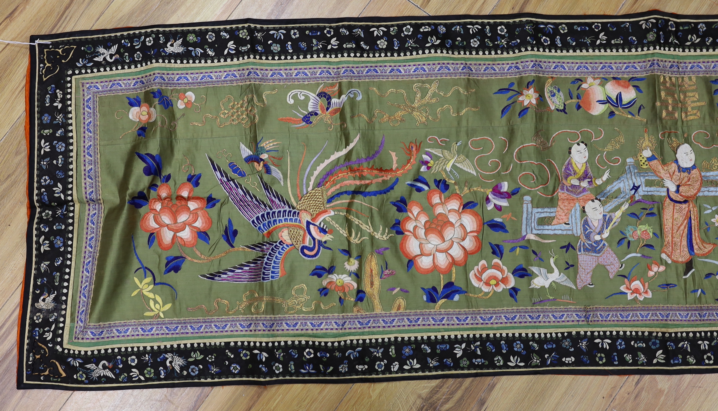 A long Chinese silk embroidered runner embroidered with the figure of Fu and boys, symbolic peaches, phoenix and flowers, possibly an altar cloth together with two other smaller runners, largest runner 202cm long x 55cm